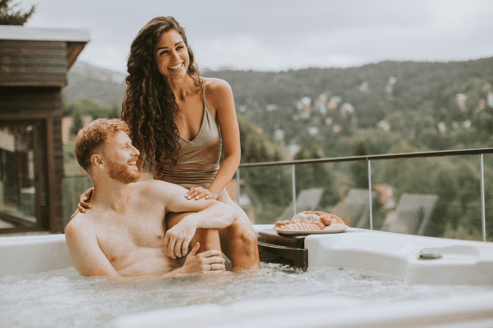 Couple enjoying an outdoor hot tub overlooking wooded hills.